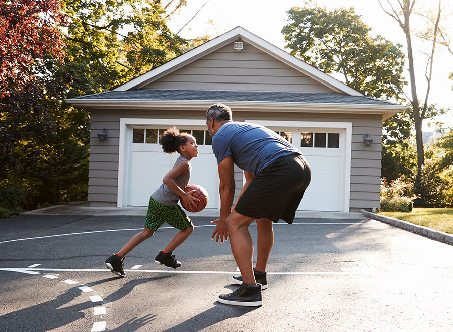 a dad and young daughter playing basketball in their driveway